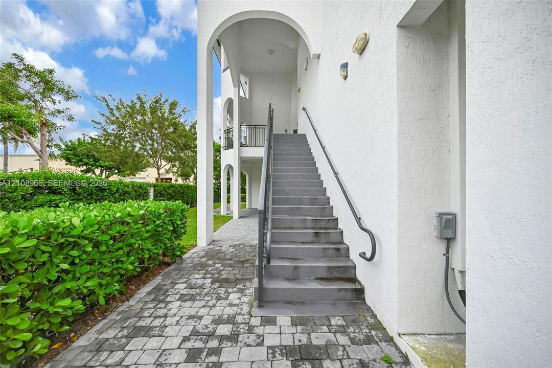 Stucco exterior featuring arched architectural elements, concrete stairs with metal railings, and stone-paver walkway