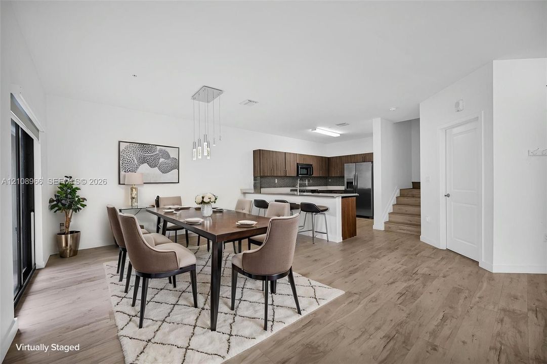 Open-concept kitchen featuring flat-panel wood-finish cabinetry, a breakfast bar with stone-finish countertops, stainless steel appliances, wood-finish flooring, and multi-pendant lighting