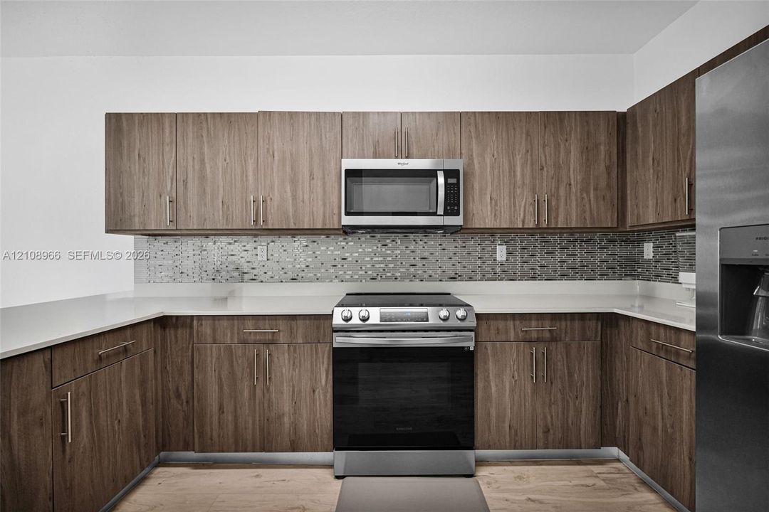 Kitchen featuring wood-finish cabinetry, stone-composite countertops, stainless steel appliances, and a glass-tile mosaic backsplash