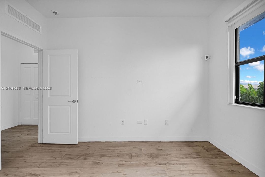 Interior space featuring wood-finish flooring, white walls, a single-panel interior door, and a multi-pane window with dark framing