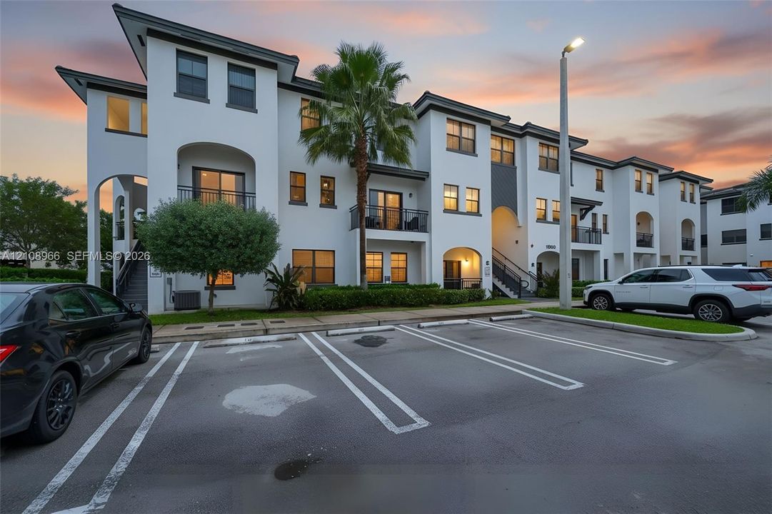 Multi-story stucco exterior with arched architectural details, private balconies, and dedicated surface parking