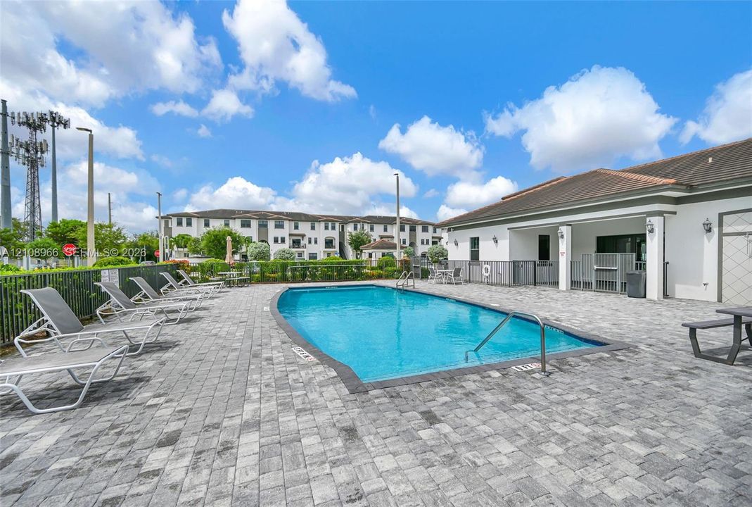 Outdoor swimming pool featuring a paver stone deck, metal handrail, and surrounding perimeter fencing