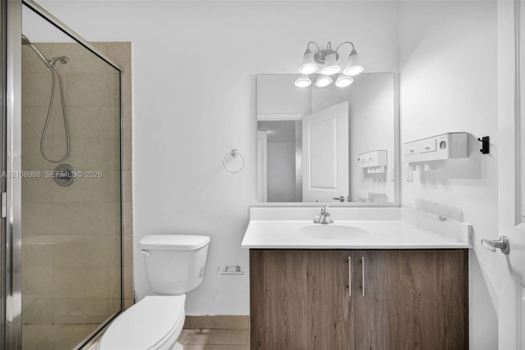 Bathroom featuring a wood-finish vanity with a white countertop, an integrated sink, a framed glass shower enclosure with tile surround, and a wall-mounted light fixture
