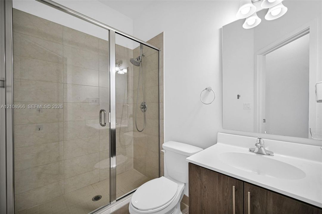 Bathroom featuring a glass-enclosed shower with tiled surround and handheld showerhead, vanity with wood-finish cabinetry, solid-surface countertop, and integrated sink