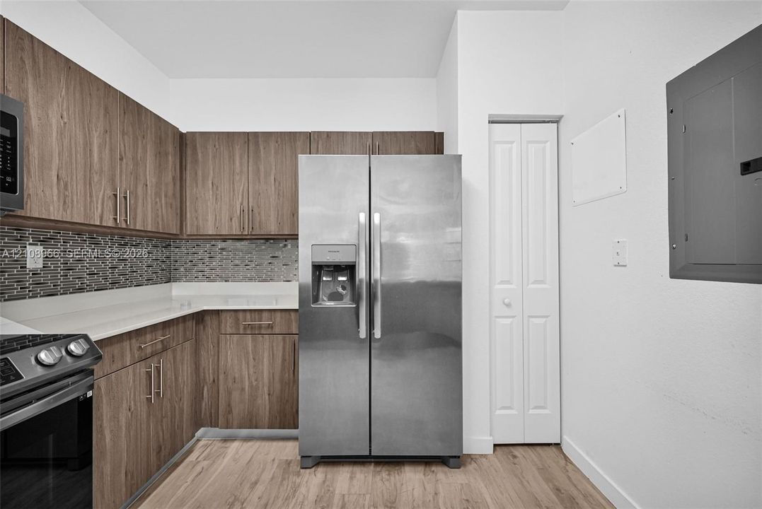 Kitchen featuring wood-finish cabinetry, stainless steel appliances, a tile backsplash, light-toned countertops, and wood-finish flooring