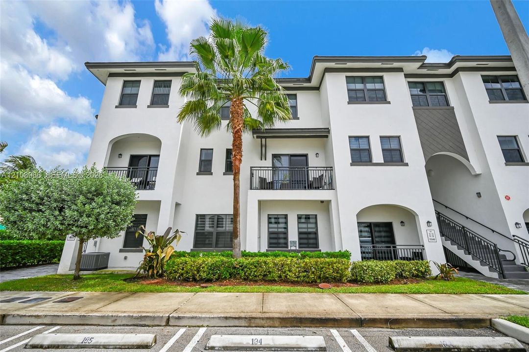 Multi-level exterior featuring white stucco finish, recessed private balconies with metal railings, dark-framed windows, and integrated landscaping
