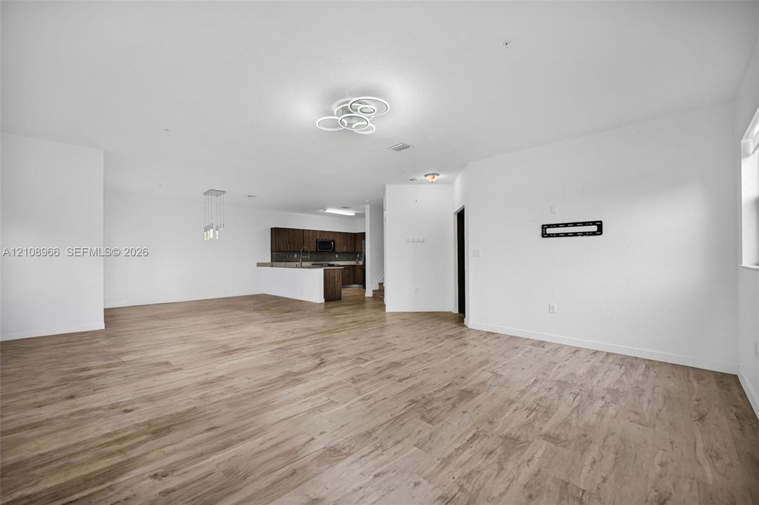 Open-concept interior featuring wood-finish flooring, contemporary multi-ring flush mount lighting, a breakfast bar with dark-toned cabinetry, and decorative pendant light fixtures
