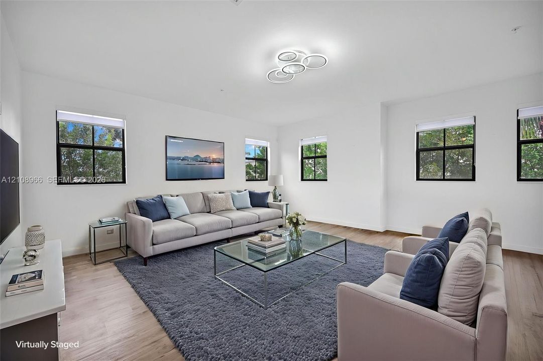 Living area featuring wood-finish flooring, multiple windows with black trim, and a modern circular tiered flush-mount light fixture