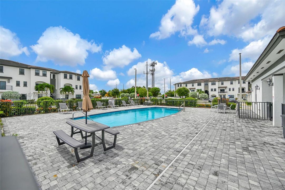 In-ground swimming pool surrounded by a grey paver deck and black metal perimeter fencing