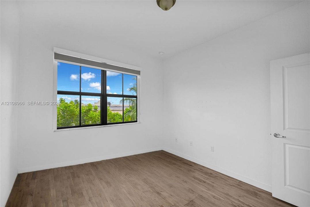 Neutral-toned room featuring wood-finish flooring, a large window with black framing, and a multi-panel interior door with brushed metal hardware