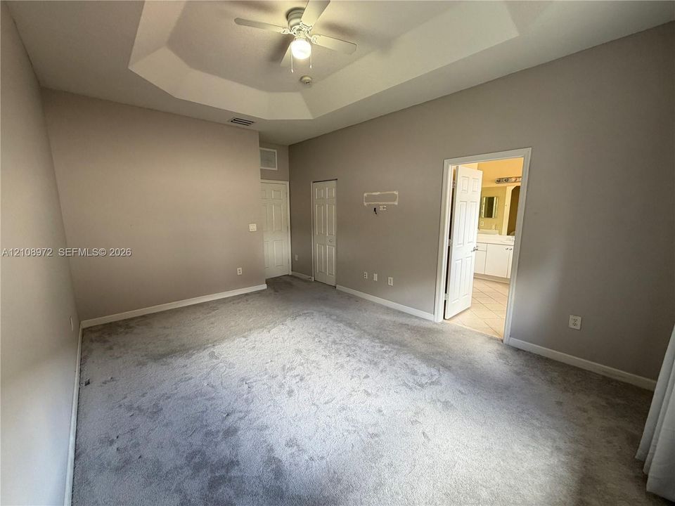 Room featuring a tray ceiling, ceiling fan with integrated light, carpeted flooring, and two interior doors