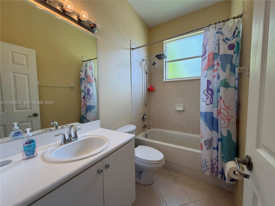 Full-width vanity with solid-surface countertop and integrated oval sink, porcelain bathtub with tile surround, polished chrome fixtures, and large wall-mounted mirror