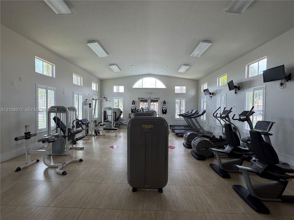Fitness center featuring tile flooring, multi-pane windows with plantation shutters, vaulted ceilings, and recessed lighting