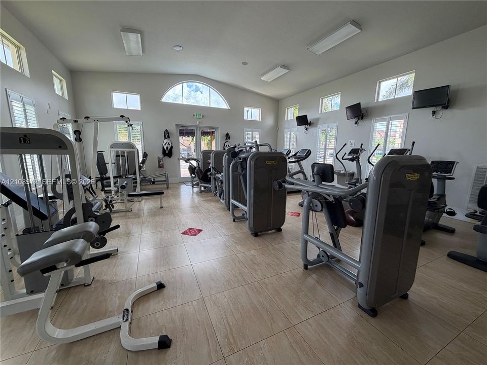 Fitness center featuring large-format tile flooring, vaulted ceilings with recessed lighting, and multiple windows including an arched architectural accent