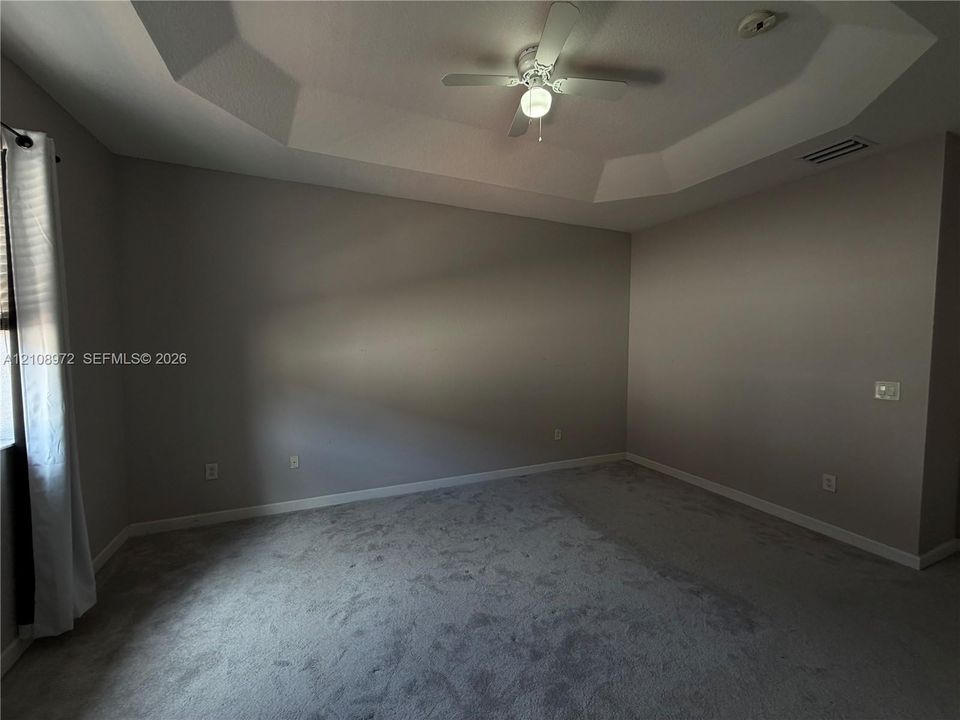 Room featuring a recessed tray ceiling, wall-to-wall carpeting, and a ceiling fan with integrated lighting
