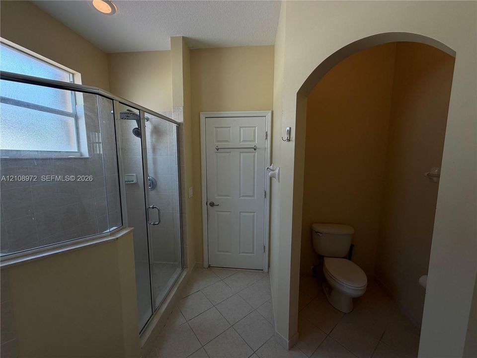 Walk-in glass shower enclosure, arched entryway to water closet, tile flooring, and recessed ceiling lighting
