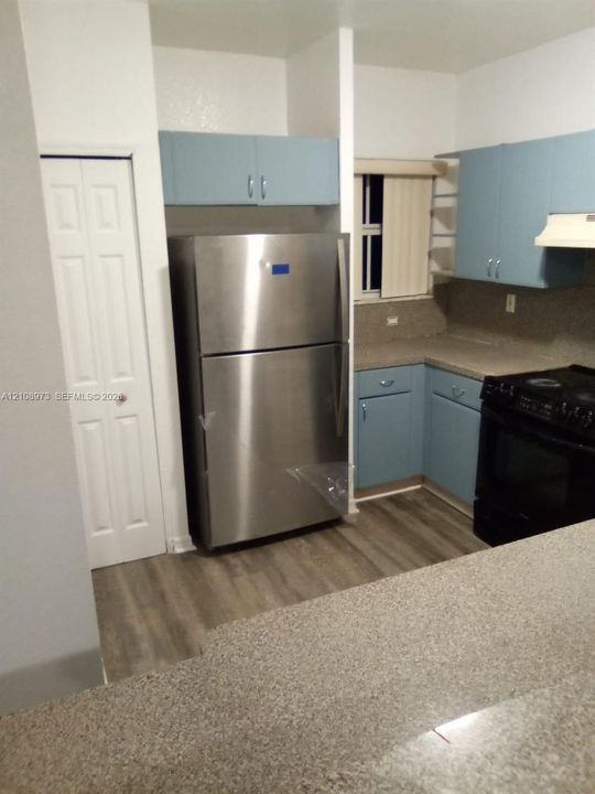 Kitchen featuring blue cabinetry, stone-finish countertops, wood-finish flooring, and a stainless steel refrigerator