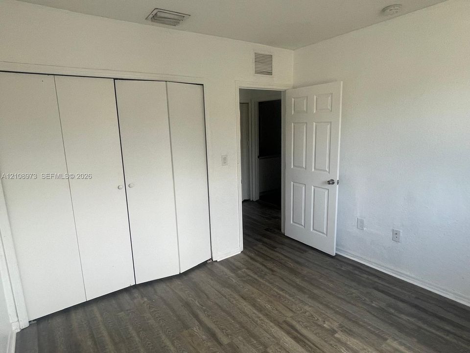 Interior room featuring wood-finish flooring, white walls, and a four-panel closet with dual-knob hardware