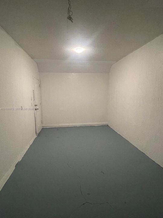 Enclosed interior space featuring textured white walls, painted concrete flooring, and a single-panel door