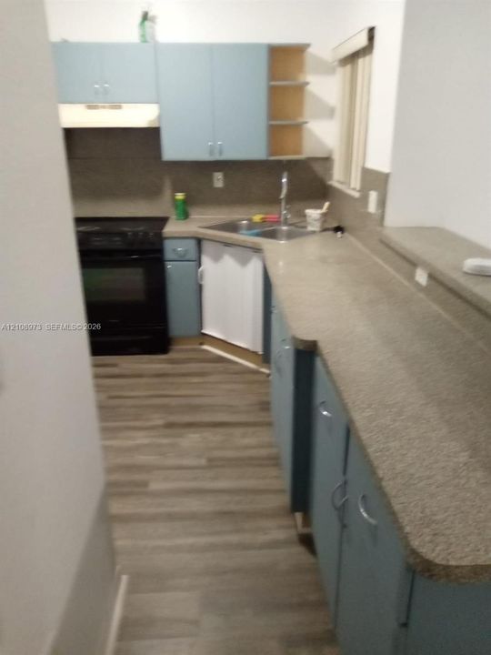 Kitchen featuring blue cabinetry, stone-finish countertops, wood-finish flooring, a stainless steel double-basin sink, and a black electric range