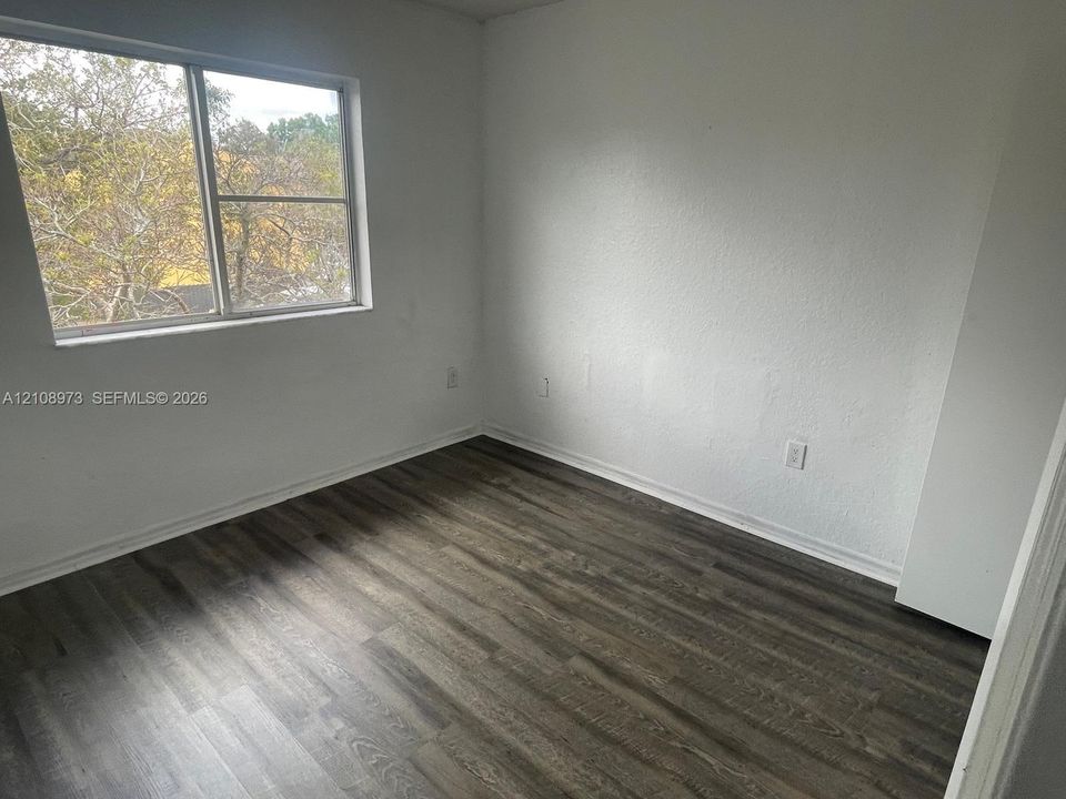 Room featuring wood-finish flooring, white walls, and a large window