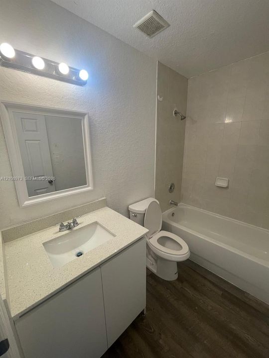 Bathroom featuring a vanity with a light-toned countertop, undermount sink, four-light vanity fixture, wall-mounted mirror, and wood-finish flooring