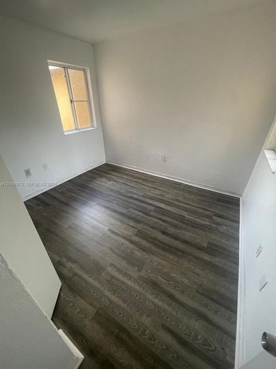 Neutral interior space featuring wood-finish flooring, smooth white walls, and a single-pane sliding window