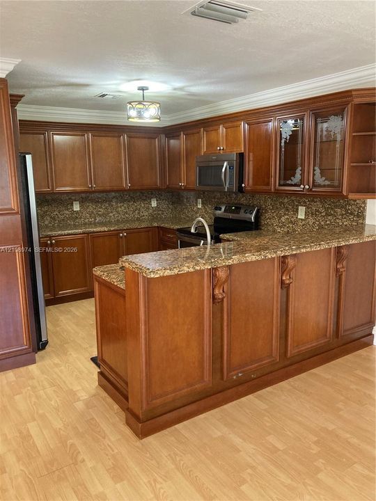 Kitchen featuring stained wood cabinetry, stone-surface countertops, decorative corbel details, glass-front upper cabinets, and wood-finish flooring