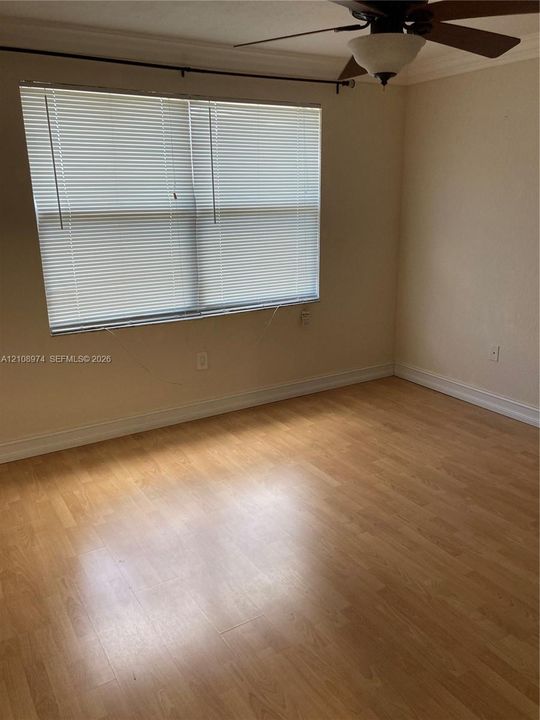 Wood-finish flooring, neutral wall tones, crown molding, double-hung window with fitted blinds, and ceiling fan with integrated light fixture