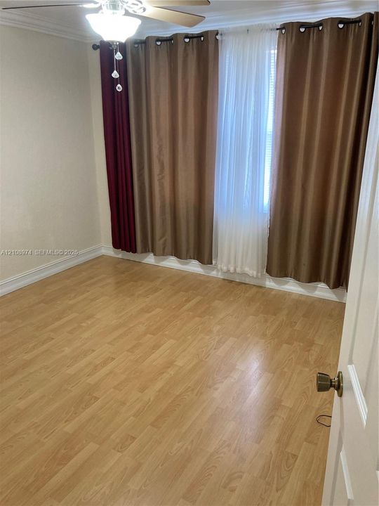 Room featuring wood-finish flooring, crown molding, and a ceiling-mounted light fixture with a fan