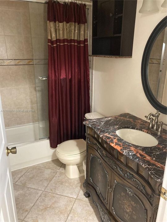 Bathroom featuring a dark-finish ornate vanity with a stone countertop, oval undermount sink, shower-tub combination with tile surround, and diamond-pattern floor tiling