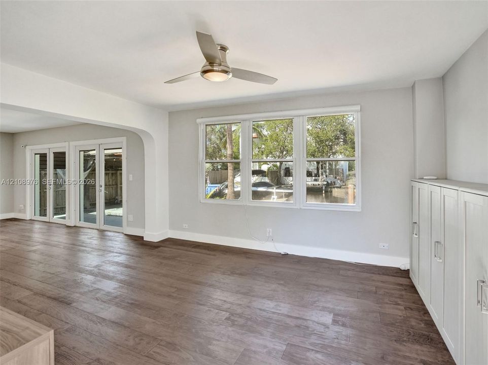 Open living area featuring wood-finish flooring, a contemporary ceiling fan with integrated lighting, triple-pane window configuration, and built-in white cabinetry