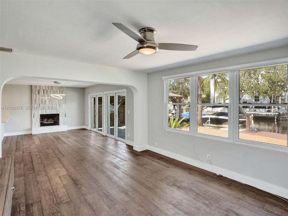 Wood-finish flooring, fireplace with vertical tile surround, recessed ceiling fan with integrated lighting, and multiple windows with water frontage