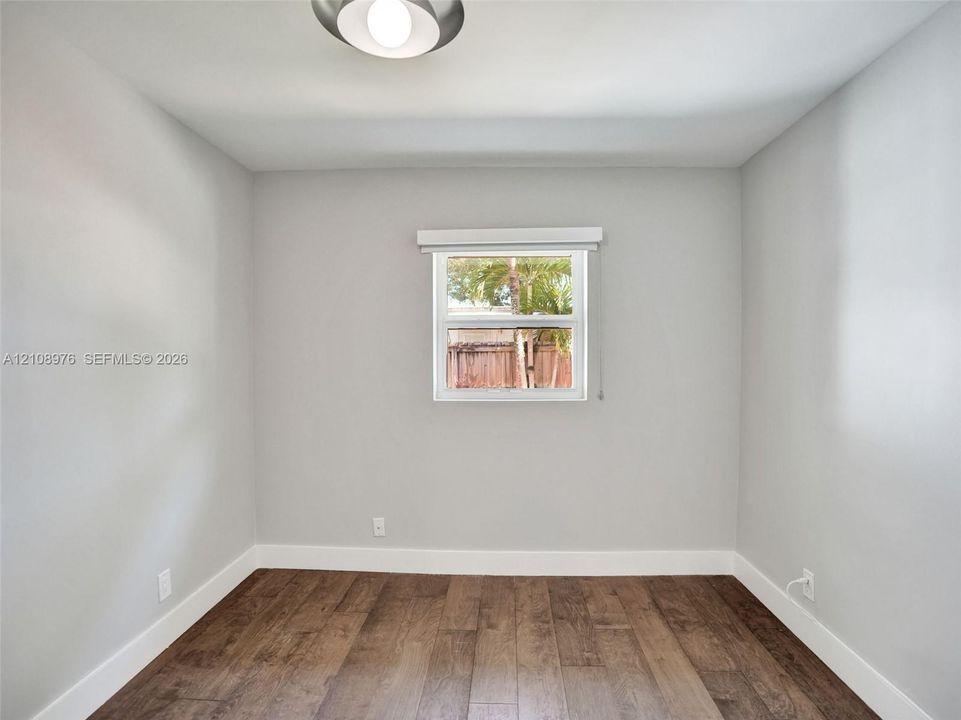 Bedroom 3. Neutral wall paint, wood-finish flooring, and single-pane window with installed window treatment, complemented by a flush-mount ceiling fixture