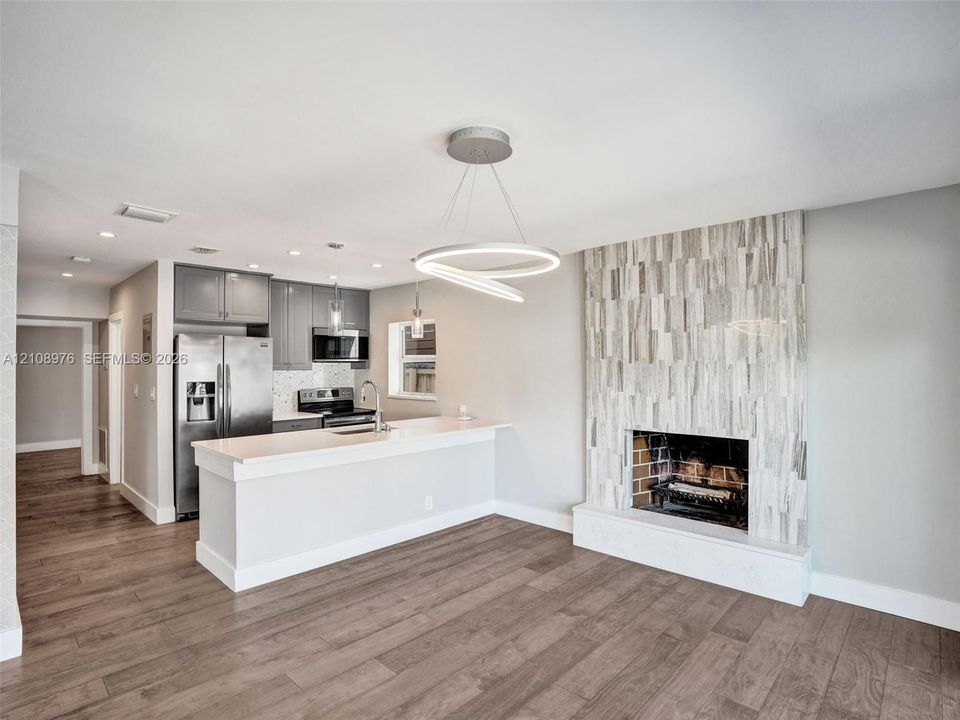Open concept interior featuring wood-finish flooring, a kitchen with quartz countertops and stainless steel appliances, and a floor-to-ceiling textured stone fireplace surround