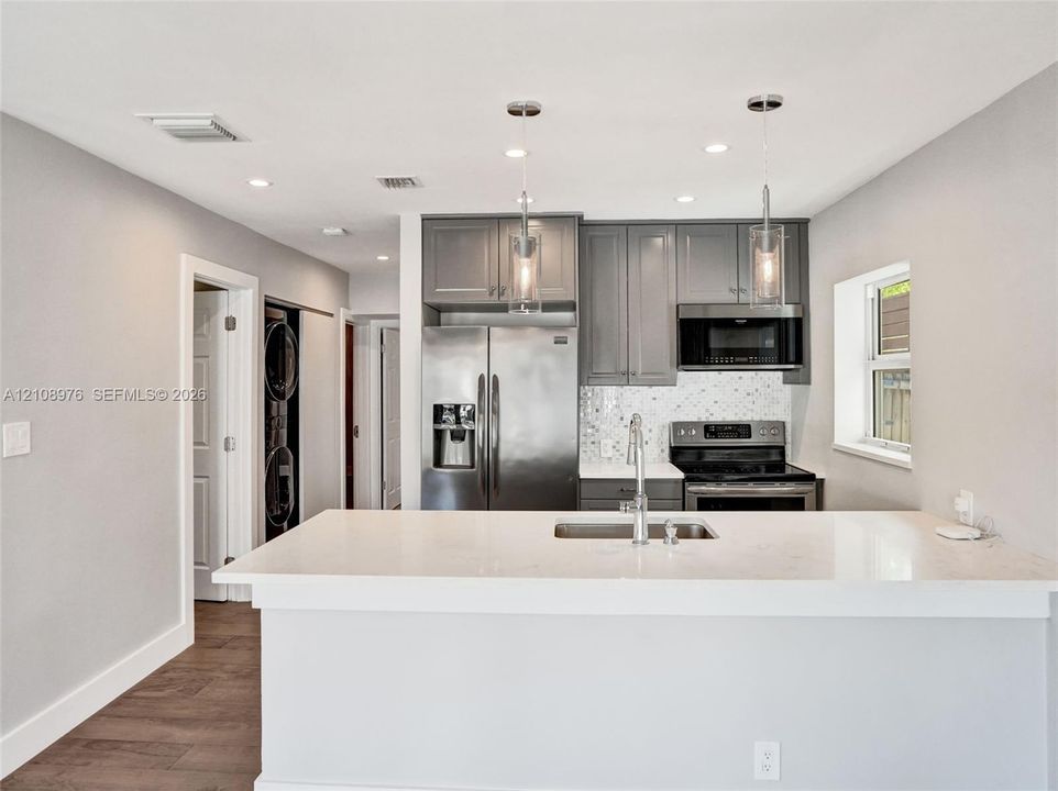 Kitchen featuring gray cabinetry, stainless steel appliances, white quartz countertops, mosaic tile backsplash, and dual pendant lighting