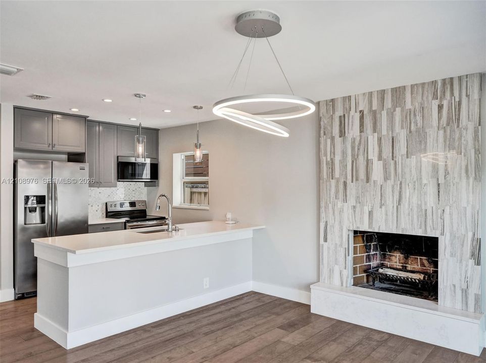Kitchen featuring grey cabinetry, stainless steel appliances, and a peninsula with a quartz countertop, complemented by a floor-to-ceiling fireplace with stone veneer surround and wood-finish flooring