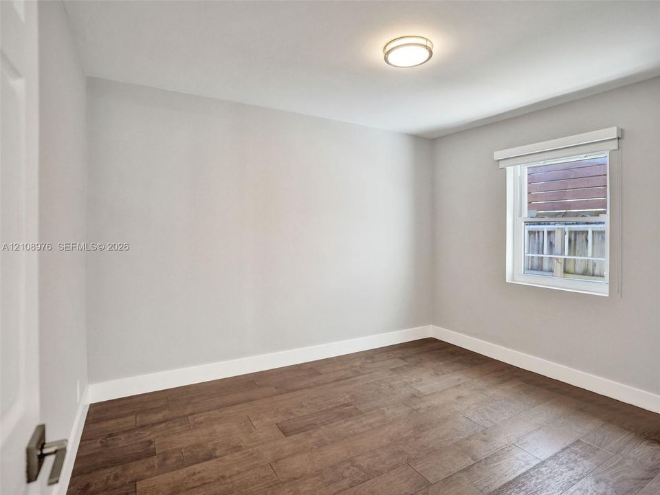 Bedroom 2. Interior space featuring neutral wall paint, wood-finish flooring, a flush-mount ceiling light fixture, and a single-hung window with a roller shade