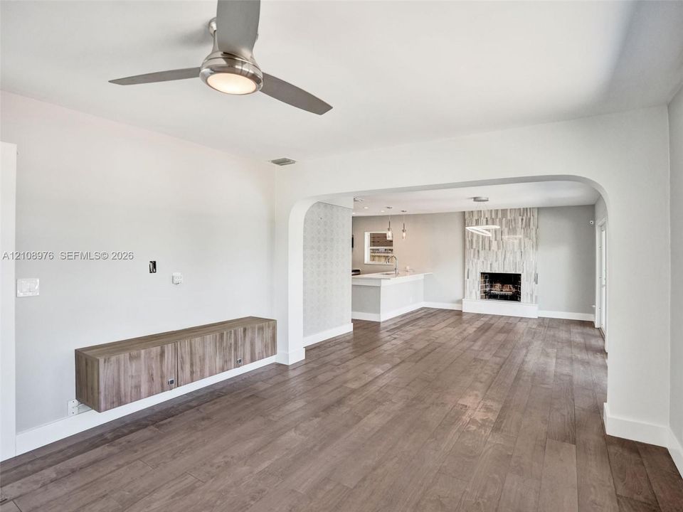 Wood-finish flooring, brushed-nickel ceiling fan with integrated lighting, wall-mounted wood-finish cabinetry, arched entryway, and fireplace with vertical tile surround