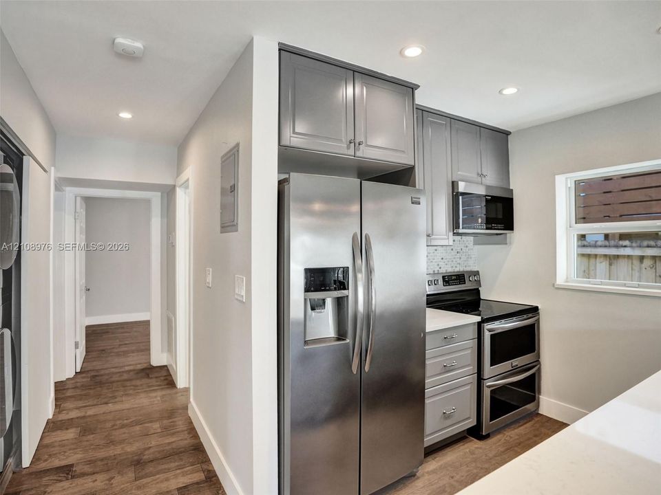 Kitchen featuring grey shaker-style cabinetry, stainless steel side-by-side refrigerator, double wall oven, quartz countertops, and recessed lighting