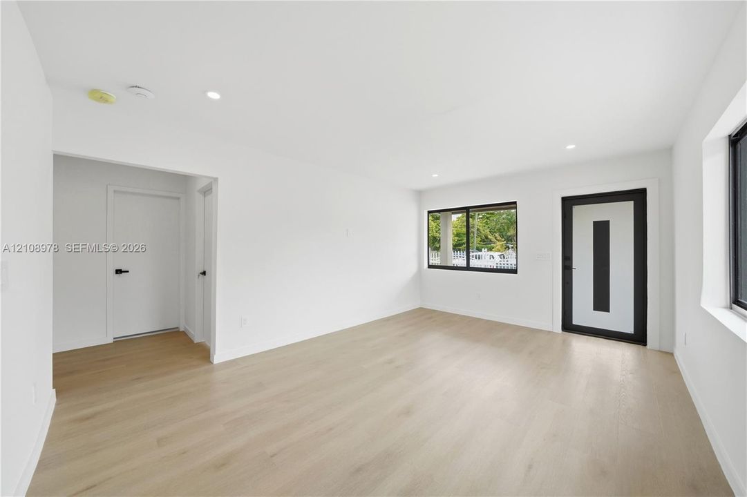 Interior space featuring wood-finish flooring, recessed lighting, white walls, black-framed windows, and an exterior door with a vertical frosted glass panel
