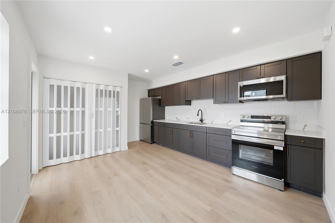 Kitchen featuring charcoal-toned cabinetry, light-toned wood-finish flooring, white stone-finish countertops, stainless steel appliances, and a glass-paneled accordion door