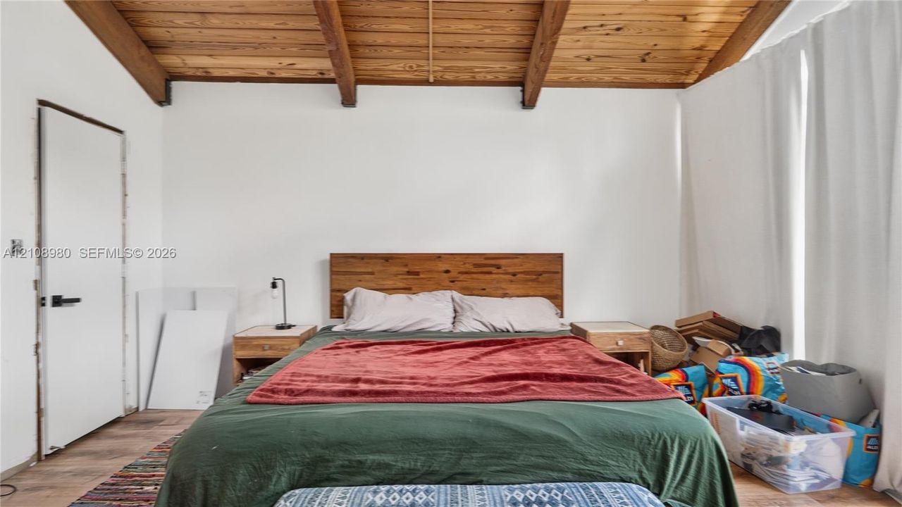 Vaulted ceiling featuring exposed wood beams, wood-finish flooring, and a flat-panel interior door with matte black hardware