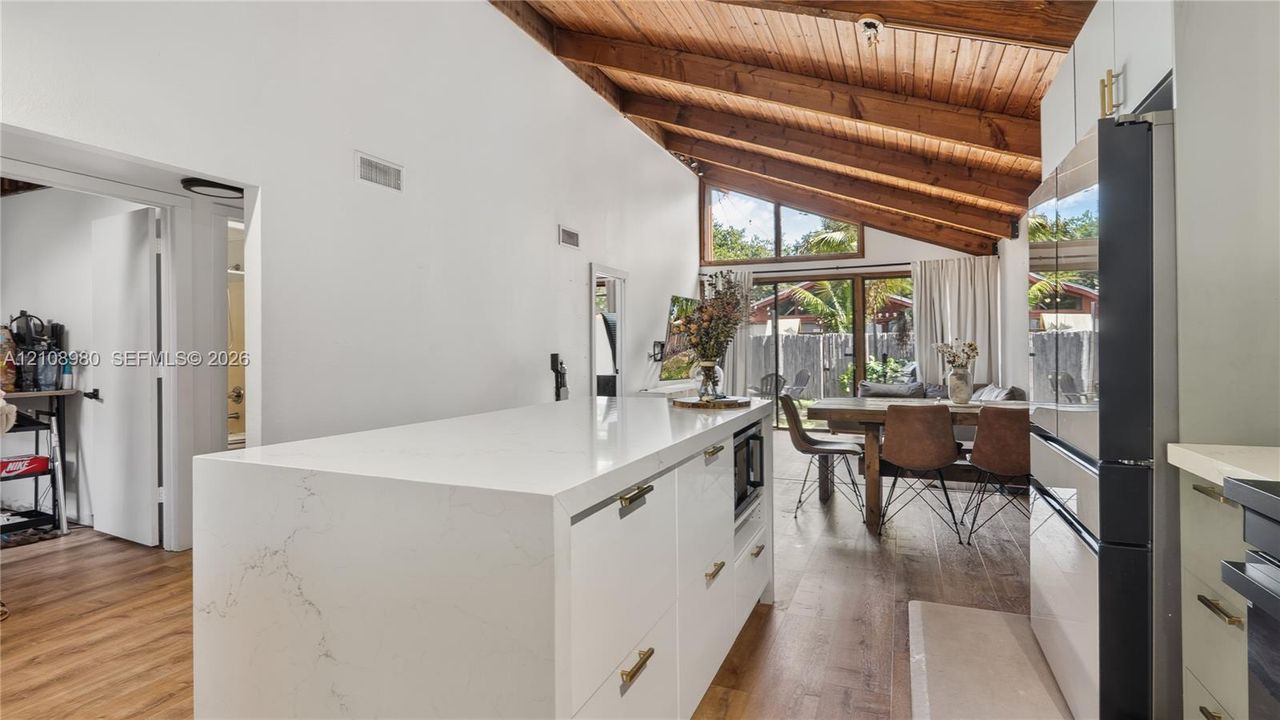 Vaulted ceilings with exposed timber beams, center kitchen island with a quartz waterfall countertop, wood-finish flooring, and floor-to-ceiling windows