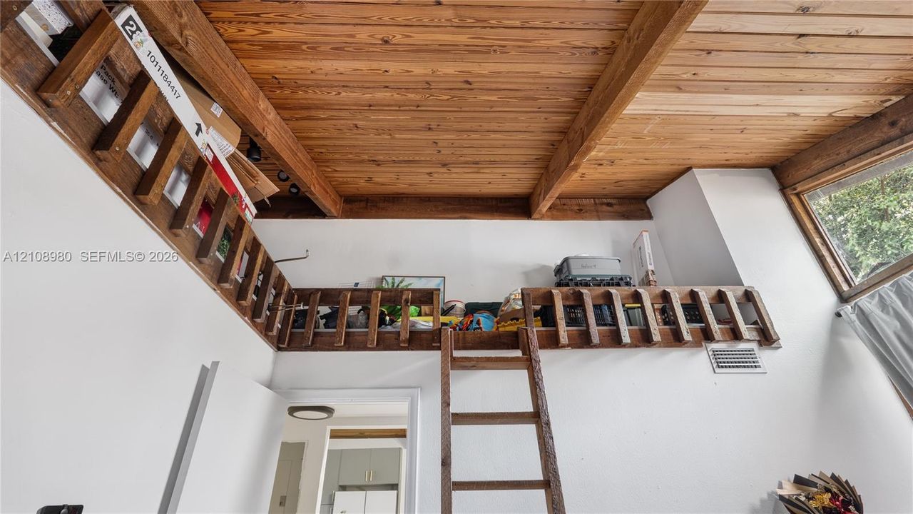 Interior space featuring high ceilings with exposed wood beams and wood-plank ceiling finish, an elevated wooden loft platform with integrated wood railings, and a wooden ladder