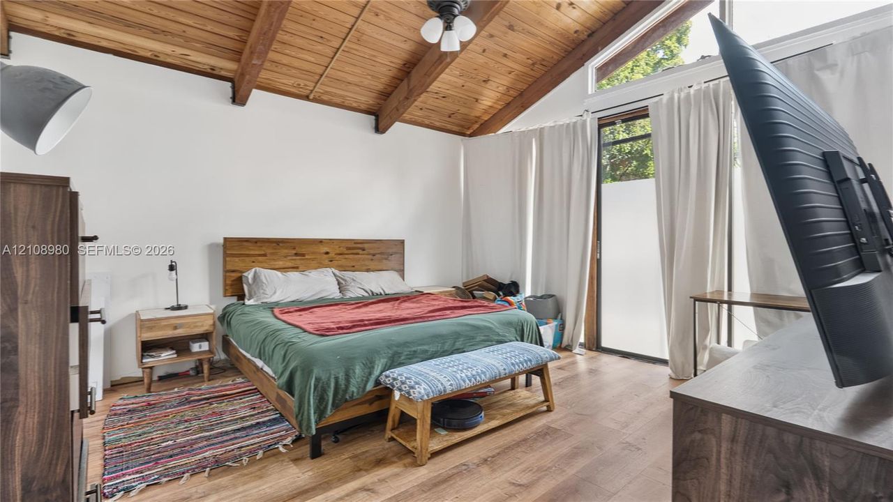 Vaulted ceiling featuring exposed wood beams, wood-finish flooring, and a glass-paneled exterior door with integrated transom window