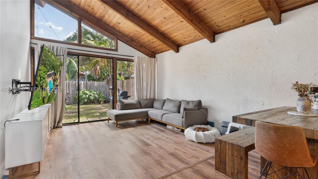 Vaulted ceilings featuring exposed wood beams, wood-finish flooring, and expansive windows with sliding glass doors