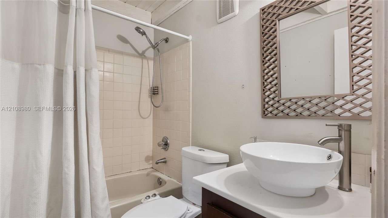 Bathroom featuring a vanity with a white vessel sink, a tall metallic faucet, a tiled shower-tub combination with a handheld showerhead, and a framed mirror