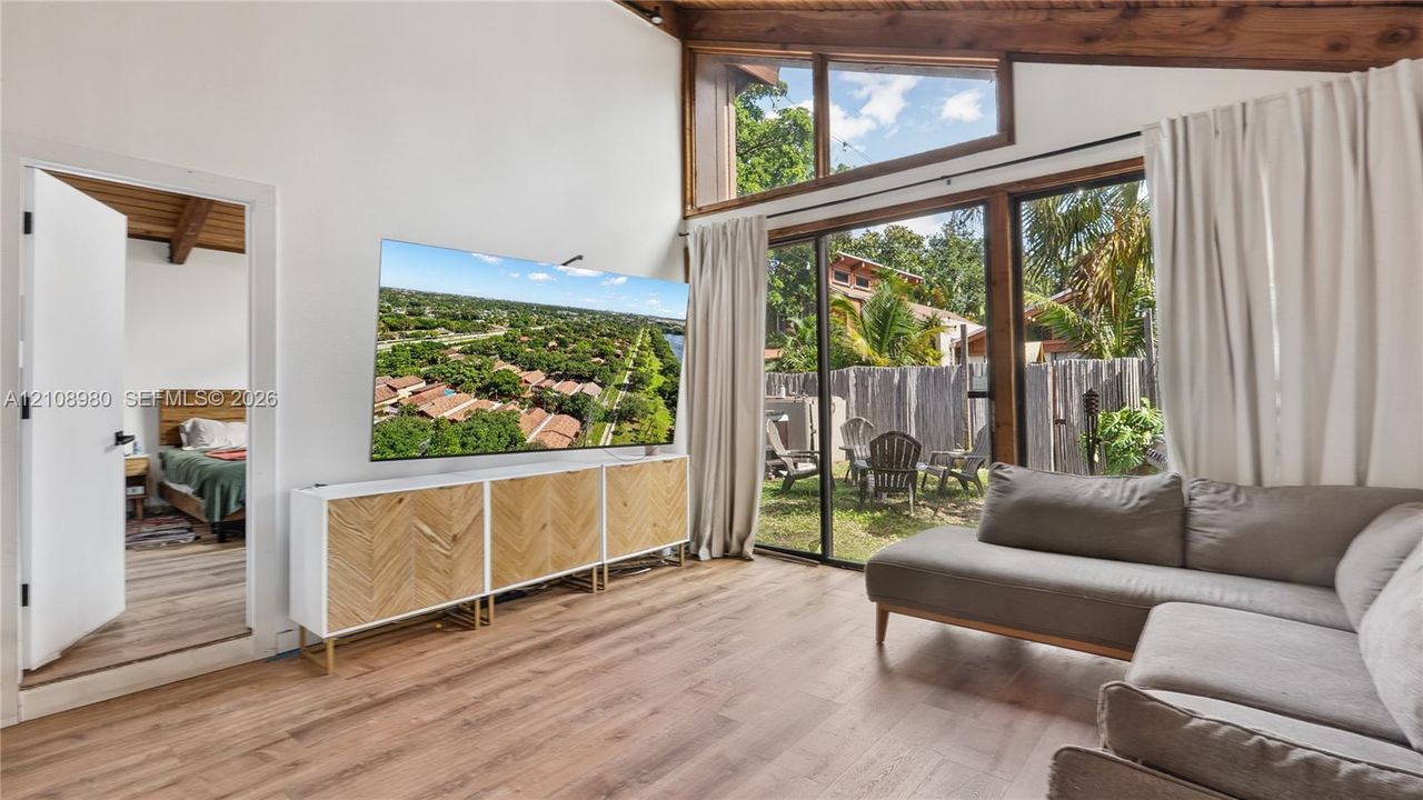 Vaulted ceilings with exposed timber beams, expansive floor-to-ceiling windows, wood-finish flooring, and sliding glass doors