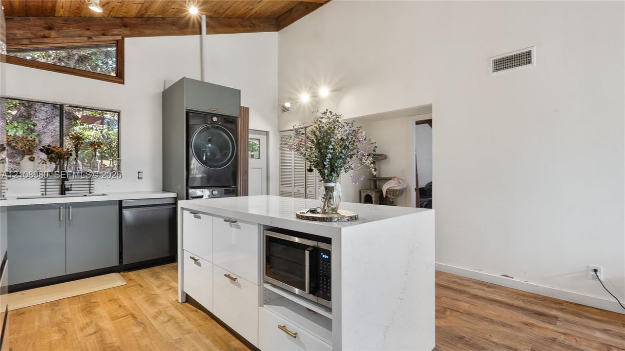 Vaulted ceiling featuring exposed wood beams, center island with stone-surface countertop, wood-finish flooring, matte-finish cabinetry, and stainless steel built-in appliances